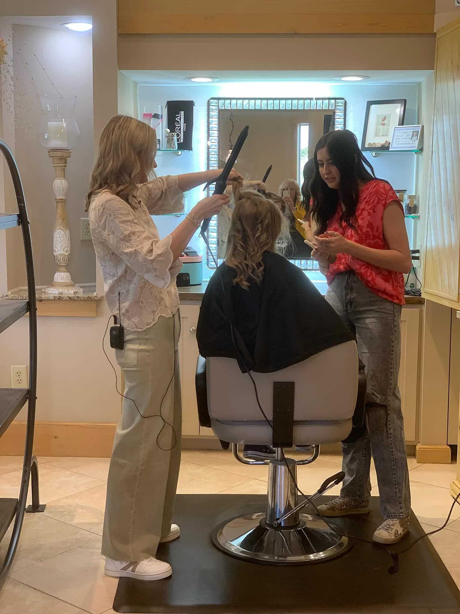 Two hairstylists curling a client's hair in a salon setting.