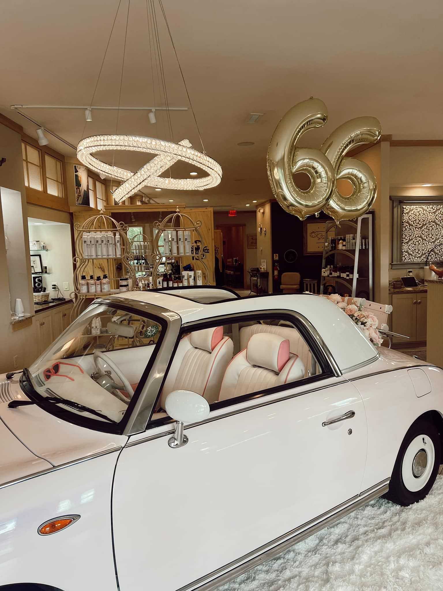 White convertible car displayed in a chic showroom with gold "66" balloons.
